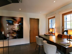 Ein modernes Interieur mit einer Holztür, einer Essecke mit Stühlen und einem Tisch sowie einem großen abstrakten Gemälde.