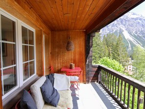 Ein hölzerner Balkon mit Blick auf Berge, einem roten Tisch und einer Couch mit Kissen.