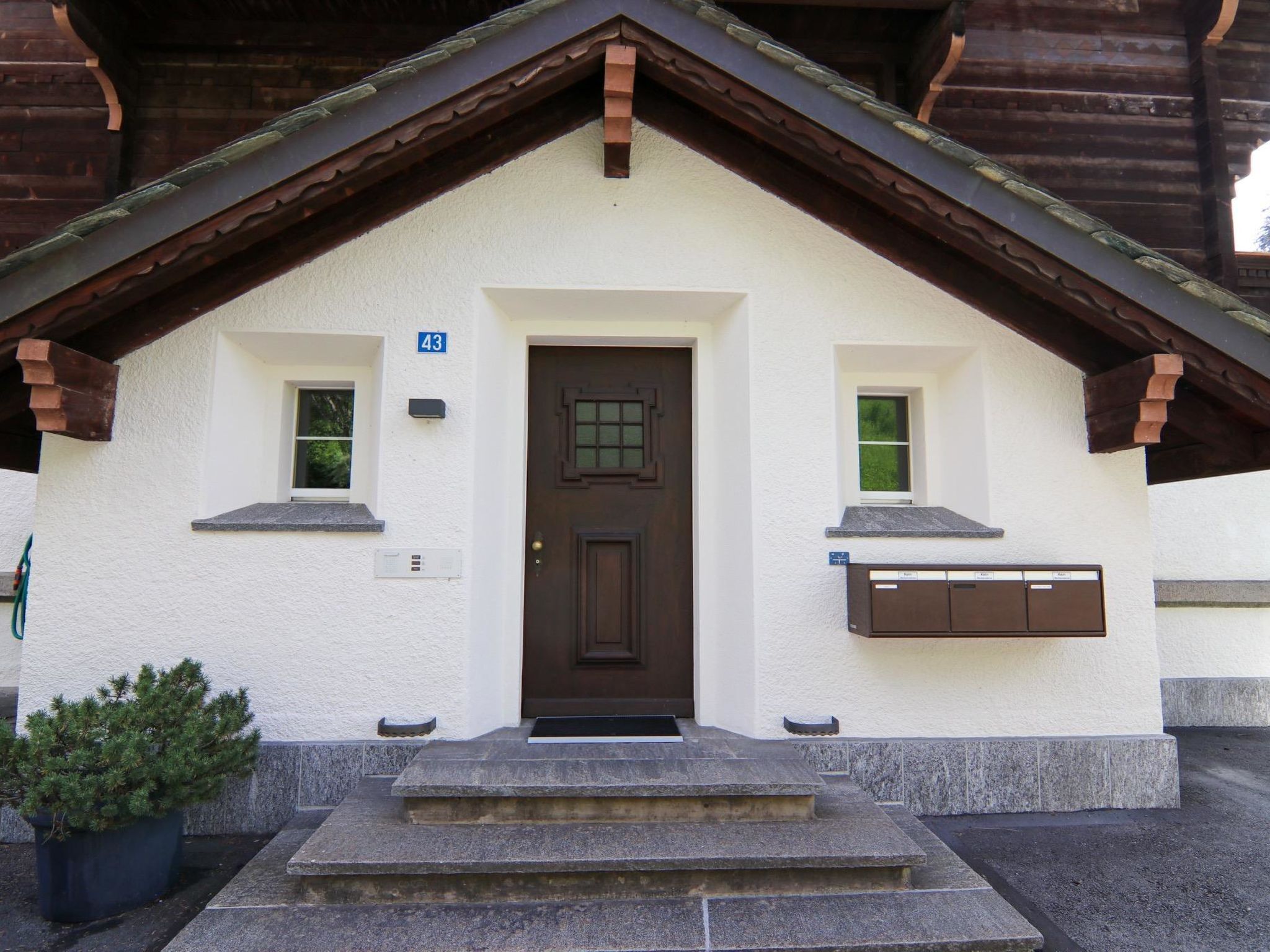 Un petit bâtiment avec une porte marron, deux fenêtres et une boîte aux lettres.