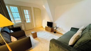 A living room with a sofa, a coffee table, a lamp, a TV, and a radiator. - Pradella 2 by Arosa Holiday Studio, Dusche und Badewanne, 4-Bettwohnung by Interhome (Arosa)