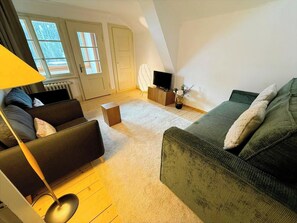 Ein Wohnzimmer mit einer Couch, einem Couchtisch, einer Lampe, einem Fernseher und einer Heizung.