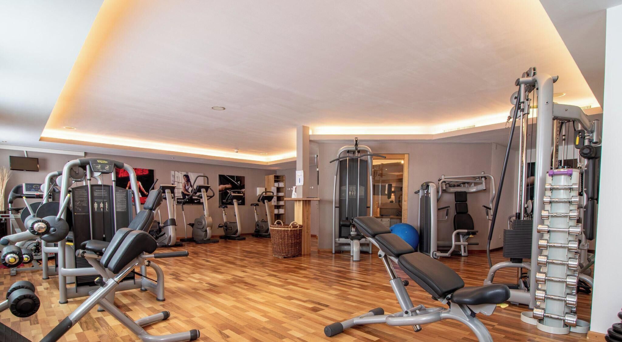 Ein Fitnessraum mit verschiedenen Trainingsgeräten, darunter Laufbänder, Crosstrainer und Gewichte.