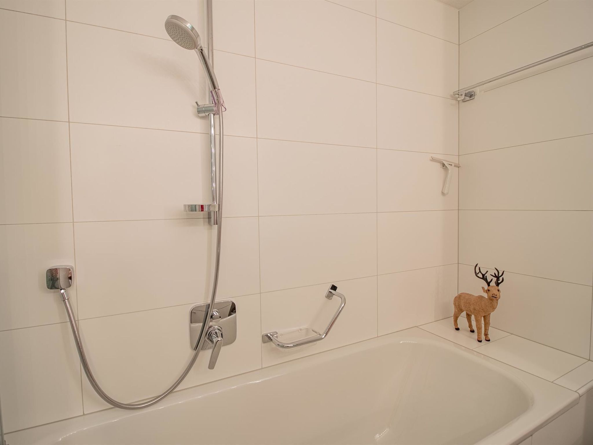 Un baño con bañera, ducha con cabezal de ducha manual y un perchero.