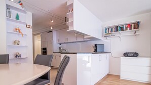 Eine moderne Küche mit weißen Schränken, ein Essbereich mit einem runden Tisch und Stühlen sowie ein Bücherregal mit Büchern und Dekoration.