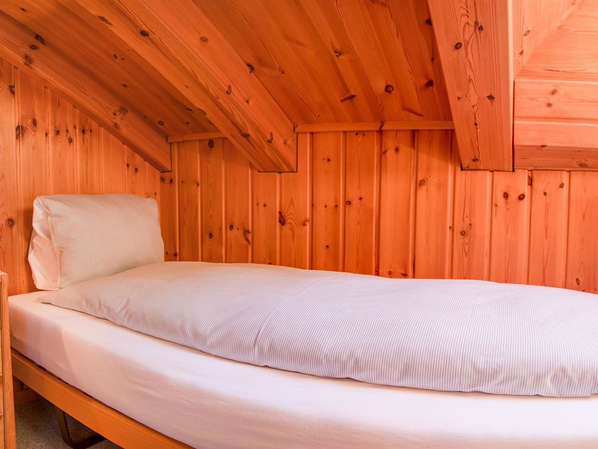 Uma cama de solteiro num quarto de madeira com teto inclinado.
