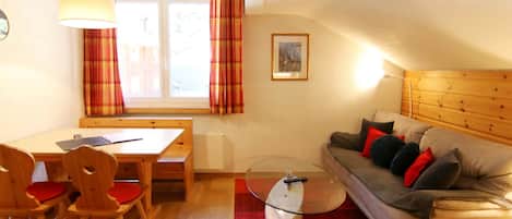 A cozy room with a wooden dining table, chairs, a sofa, and a glass coffee table.