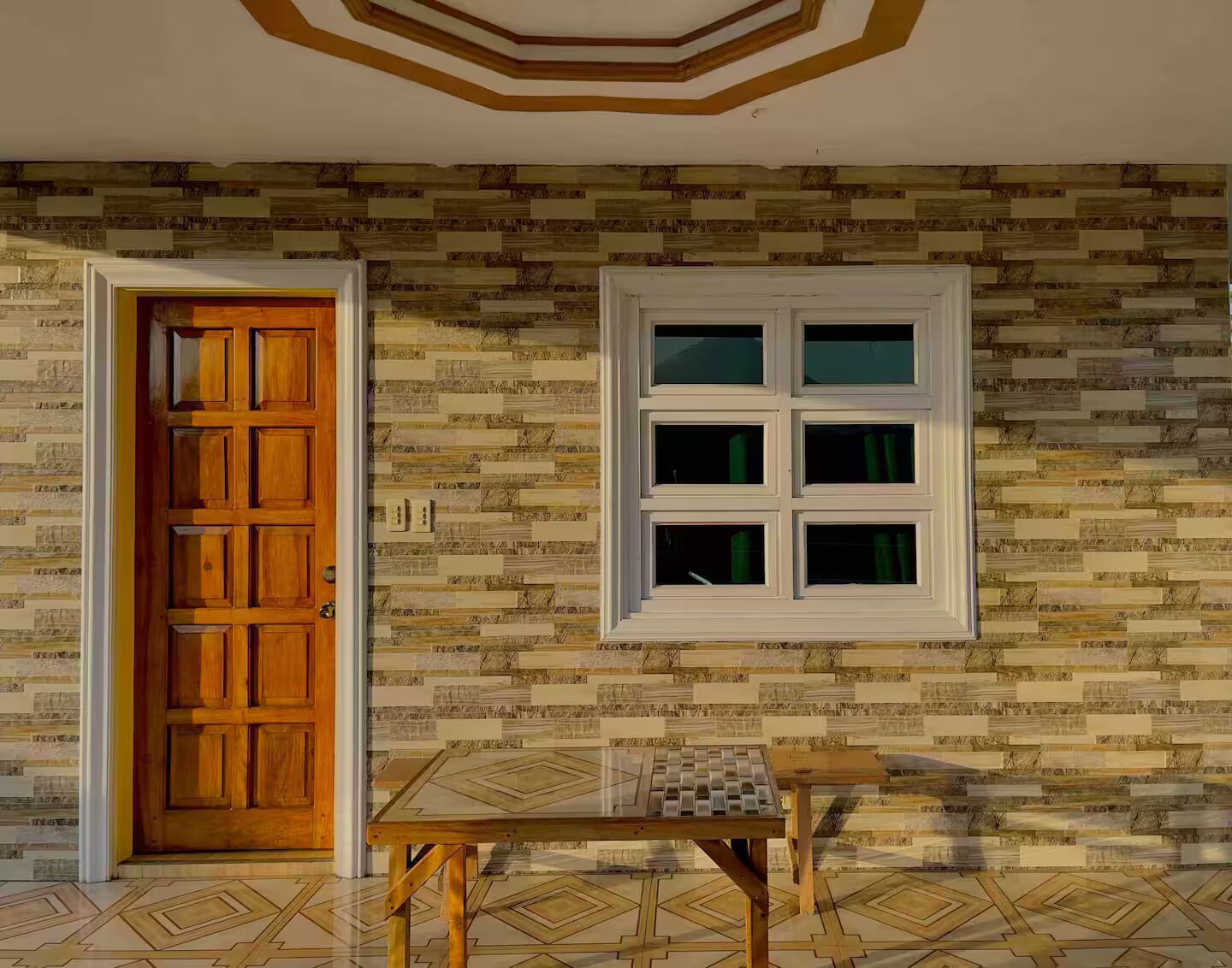 Una stanza con una porta in legno, una finestra a più vetri e un piccolo tavolo con una tovaglia a motivi geometrici.