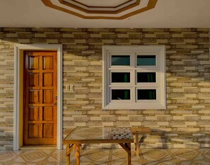 A room with a wooden door, a window with multiple panes, and a small table with a geometric patterned tablecloth.
