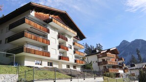 Ein mehrstöckiges Hotel mit Balkonen, einer Steinsichtmauer und einer Bergkulisse.