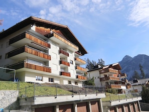Ein mehrstöckiges Hotel mit Balkonen, einer Steinsichtmauer und einer Bergkulisse.
