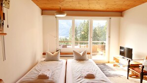 Ein Zimmer mit zwei Betten, einem Fernseher und einem großen Fenster mit Blick auf Bäume.