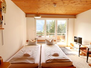 Ein Zimmer mit zwei Betten, einem Fernseher und einem großen Fenster mit Blick auf Bäume.