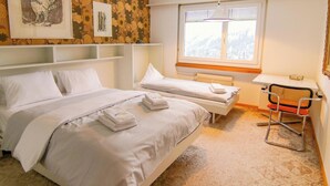 Ein Hotelzimmer mit zwei Betten, einem Fenster mit Blick auf eine verschneite Landschaft und einem Sessel.