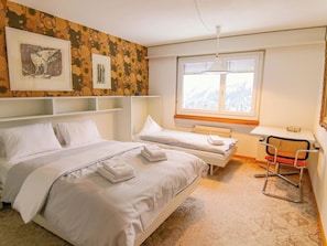 Ein Hotelzimmer mit zwei Betten, einem Fenster mit Blick auf eine verschneite Landschaft und einem Sessel.