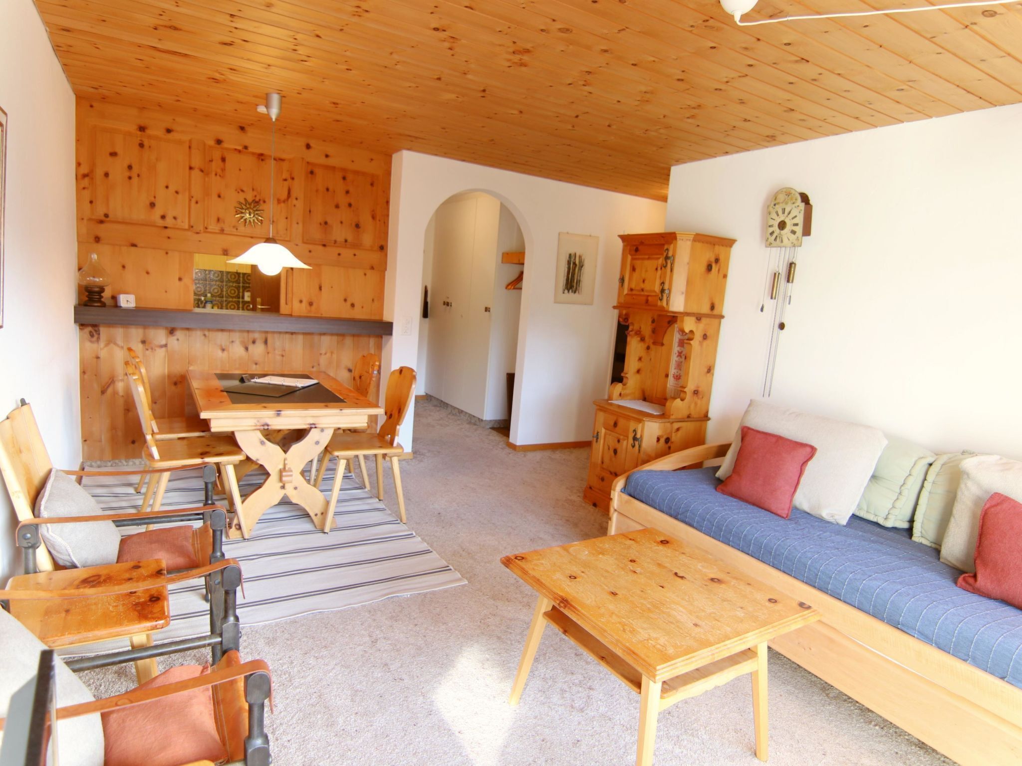 A cozy interior with a wooden dining table, chairs, a sofa, and a small wooden cabinet.