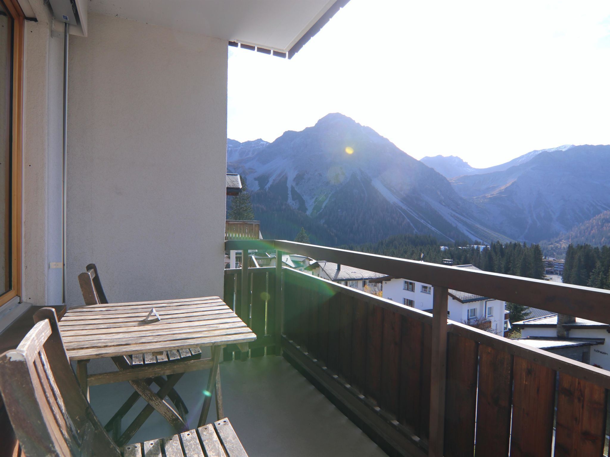 A balcony with a wooden table and chairs, overlooking a mountainous landscape.