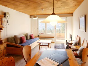 A cozy living room with a wooden ceiling, a sofa with cushions, a dining table with chairs, and a large window offering a view of the outdoors. - Dschember by Arosa Holiday Appartement/Fewo, Bad, WC, 4-Bettwohnung by Interhome (Arosa)