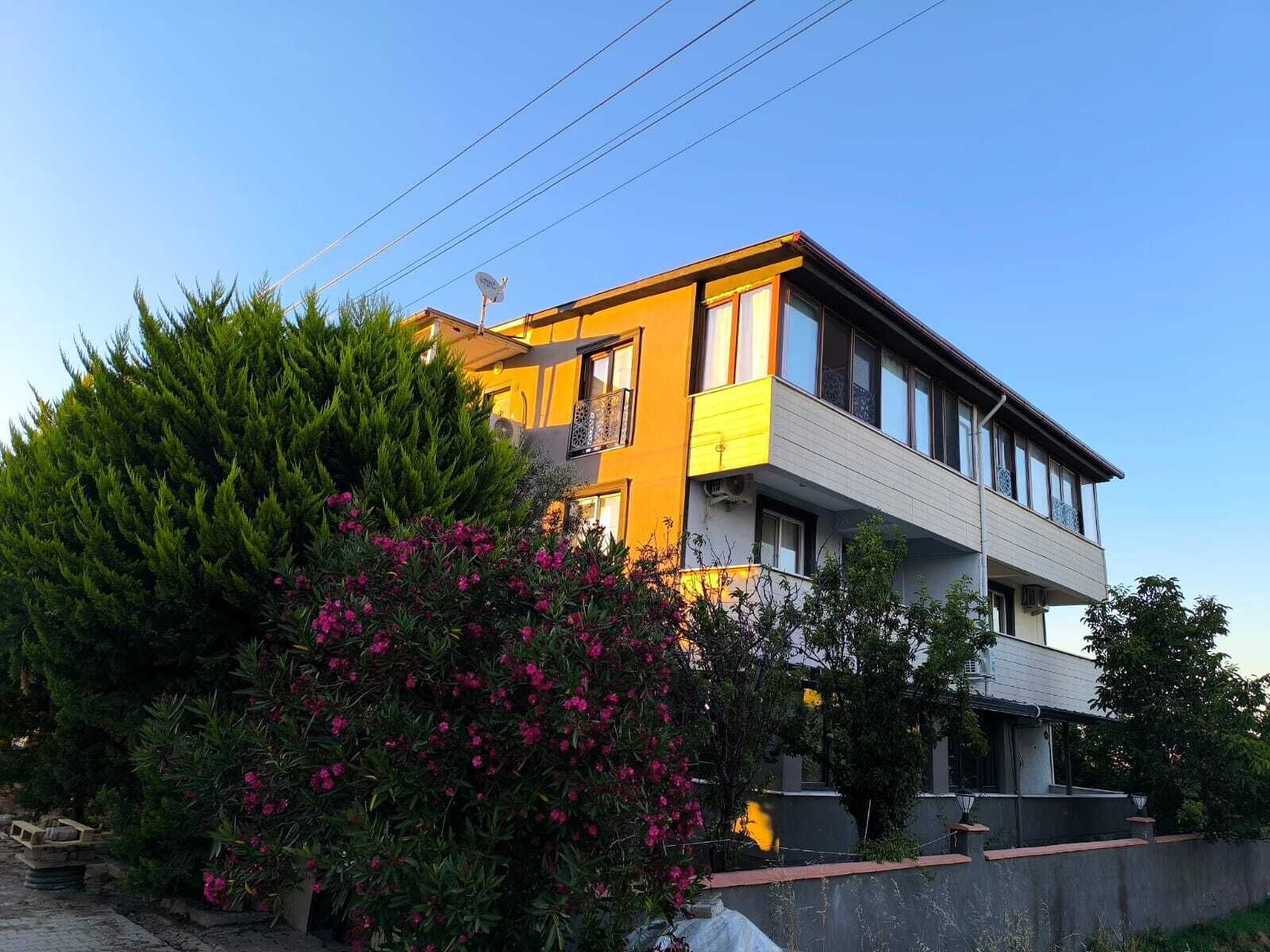 A two-story building with balconies, surrounded by greenery and flowering plants.