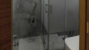 A bathroom with a glass shower enclosure, marble walls, and a wooden door frame. - Vizyon Konak (Burhaniye)