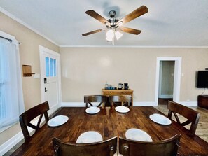 Ein Esszimmer mit Holztisch, Stühlen, Deckenventilator und einer Küchenzeile mit Schränken und einer Kaffeemaschine.