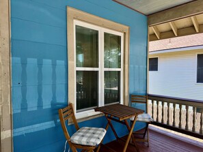 Eine Veranda mit Tisch, zwei Stühlen, einem Fenster und einem Geländer.