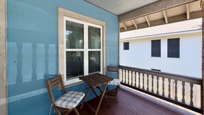 Eine überdachte Veranda mit Tisch und zwei Stühlen, einem Fenster und Blick auf einen weißen Mobilwagen.