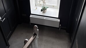 Una escalera con un radiador, una orquídea en maceta y una ventana que da a vistas exteriores.