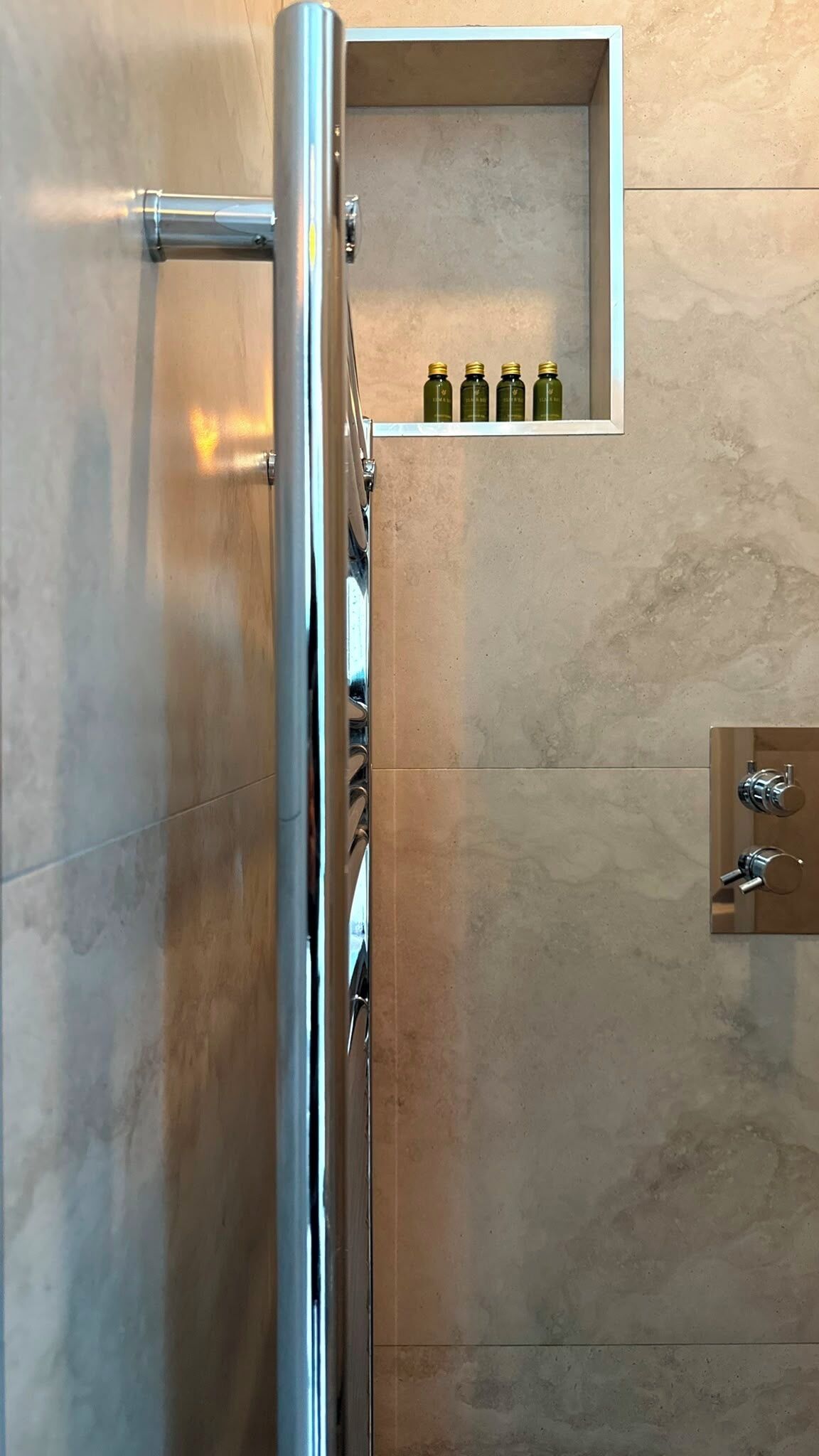 Un baño con zona de ducha, estante con botellas y un perchero para toallas.