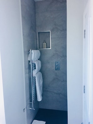 Un baño con toallero, un estante pequeño con una botella y un secador de manos.