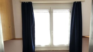 Una habitación pequeña con dos camas, una ventana con cortinas, un radiador y un armario de madera.