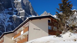 Un hotel llamado 'Gitzifurka' con una montaña cubierta de nieve al fondo y balcones de madera.