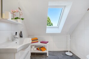 Ein modernes Badezimmer mit Oberlicht, einem weißen Waschbecken, einer Toilette und einer Dusche.