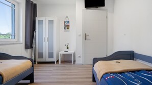 Ein Zimmer mit zwei Betten, einem kleinen Tisch, einem Kleiderschrank, einem Fernseher und einem Fenster.