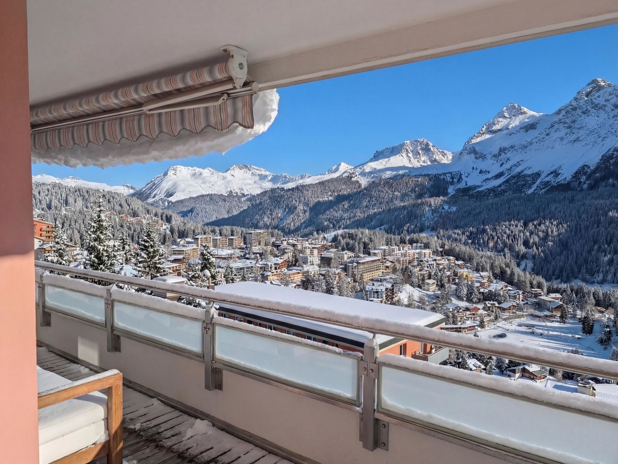 A balcony with a view of a snow-covered mountain range and a town below.