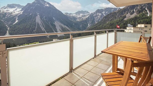 Ein Balkon mit Holztisch und Stühlen, mit Blick auf eine gebirgige Landschaft.