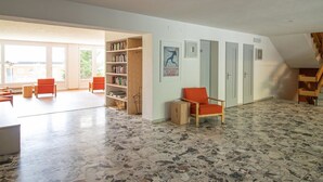 Ein geräumiger Raum mit großem Fenster, einem Bücherregal, einem roten Sessel und einer Holztreppe.