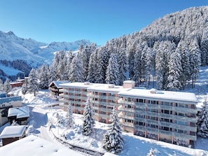 Ein mehrstöckiges Hotel inmitten einer verschneiten Landschaft, umgeben von Bergen und Bäumen.