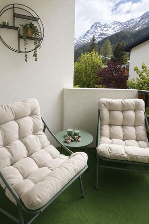 A balcony with two cushioned chairs, a small table with drinks, and a view of snow-capped mountains. - Majesta Leukerbad # 3-bed apartment, Bad, WC by Interhome (Leukerbad)