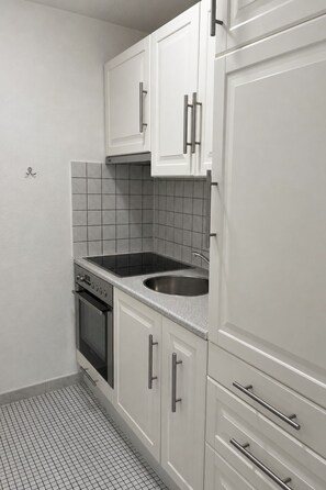 A kitchen with white cabinets, a stainless steel sink, and a black stove. - Majesta Leukerbad # 3-bed apartment, Bad, WC by Interhome (Leukerbad)