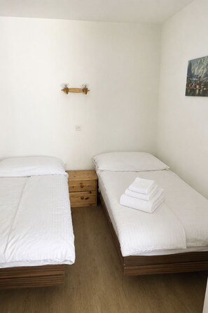 Camera da letto con due letti singoli, un comodino in legno e un punto luce a parete.
