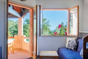 Ein Zimmer mit Balkon, einem Bett, einem kleinen Tisch und einem Fenster mit Blick auf Grünflächen und Blumen.