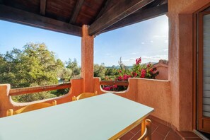 An outdoor patio with a table and chairs, surrounded by a wooden railing and a view of trees and flowers. - Vrbo Property (Zonza)