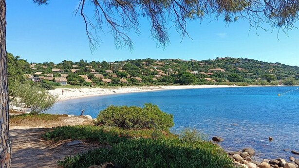 A coastal landscape with a beach, clear blue water, and a hillside with houses. - Duplex 400 meters from the ocean with a pool in a gated community (Zonza)