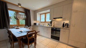Een moderne keuken met een eettafel, stoelen, een kroonluchter en uitzicht op de omgeving.