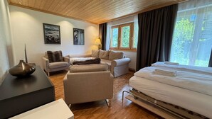 Een hotelkamer met een houten plafond, een bed, een bank, een stoel, een kleine tafel en een raam met gordijnen.