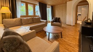 Een woonkamer met een bank, fauteuil, salontafel, houten vloer en uitzicht door grote ramen.