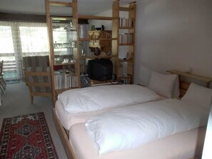 A room with a bed, a television, a bookshelf, and a window. - Valère Leukerbad # 2-bed apartment, Dusche, WC by Interhome (Leukerbad)