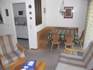 A compact living space with a kitchenette, a dining area with a checkered tablecloth, and two wooden chairs. - Valère Leukerbad # 2-bed apartment, Dusche, WC by Interhome (Leukerbad)