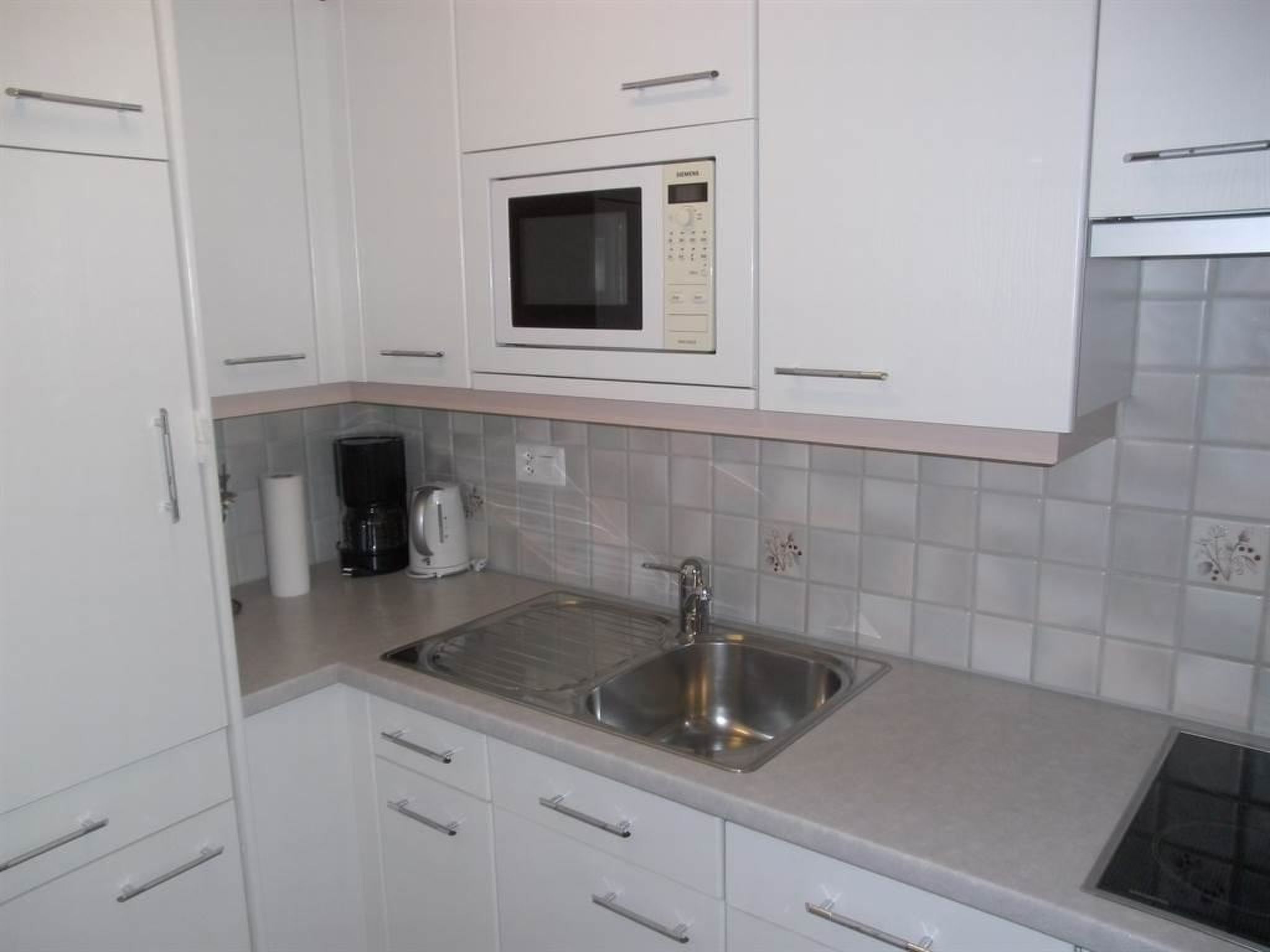 A kitchen with white cabinets, a stainless steel sink, a microwave, and a coffee maker.