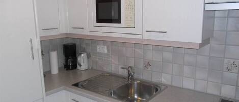 A kitchen with white cabinets, a stainless steel sink, a microwave, and a coffee maker.